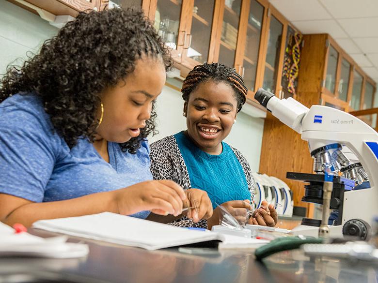 生物课上，两个女学生坐在显微镜前
